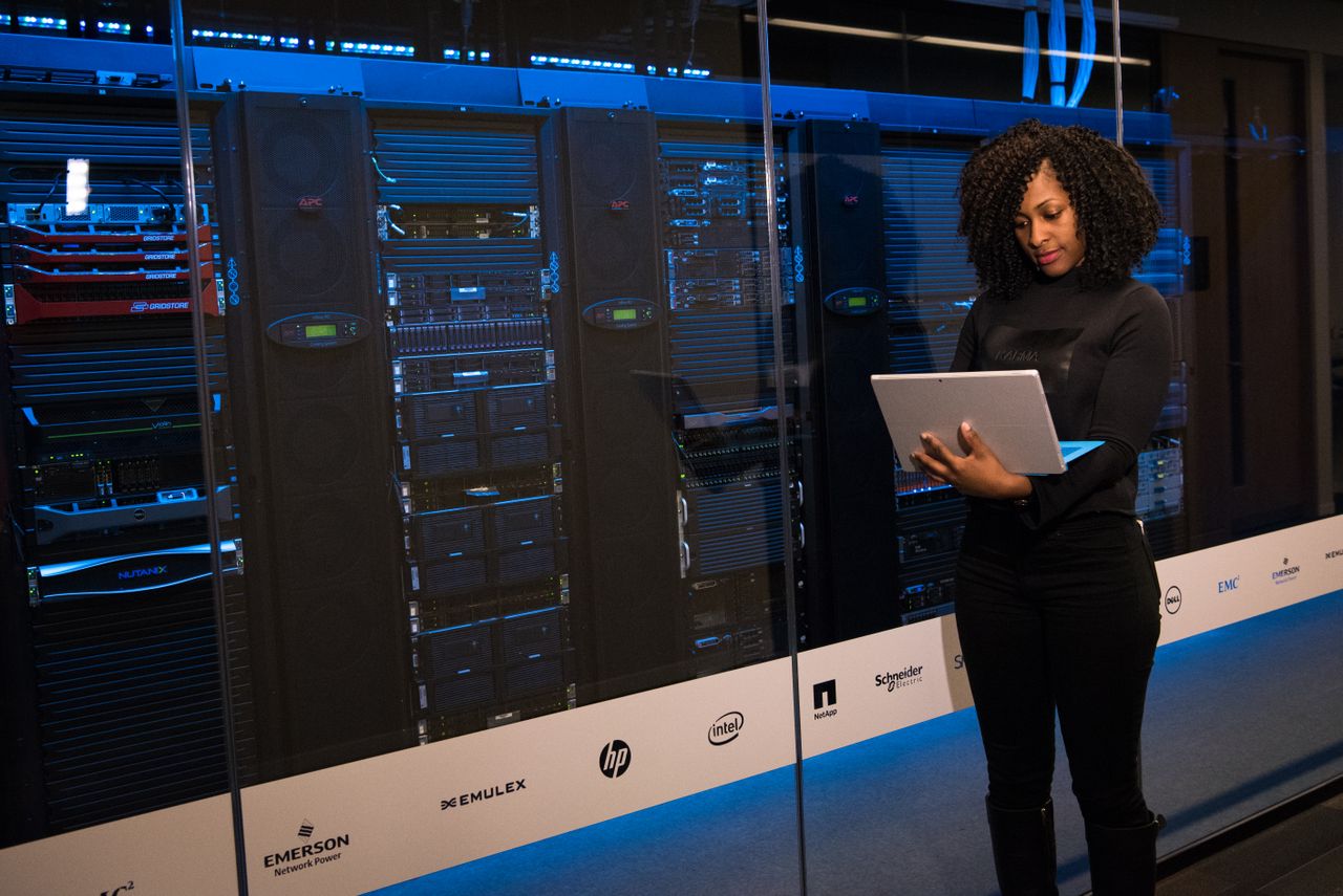 trusted-partner A female engineer using a laptop while monitoring data servers in a modern server room.