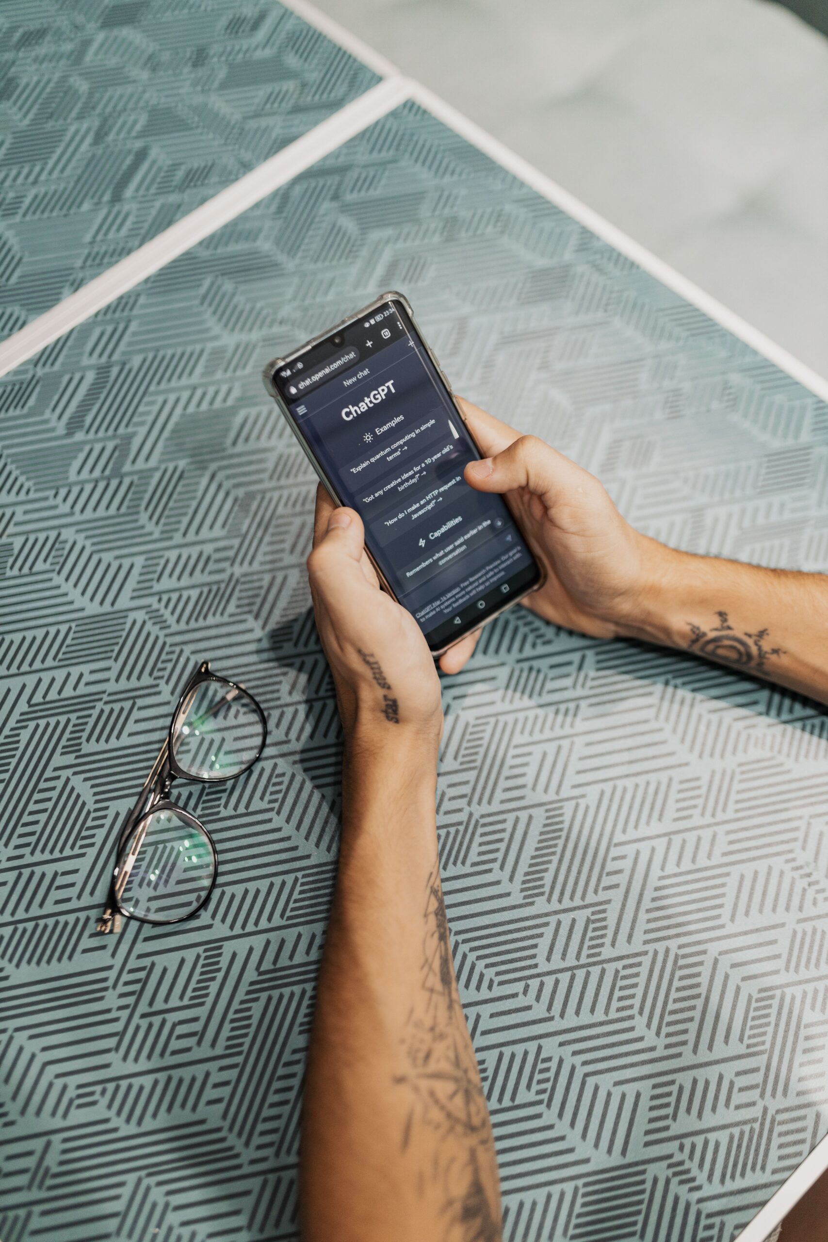 Home Hands holding smartphone displaying ChatGPT app near eyeglasses on table.