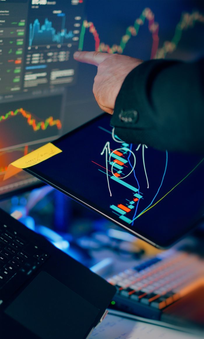services-03 A business professional examines financial charts on a tablet and monitor for investment strategy.